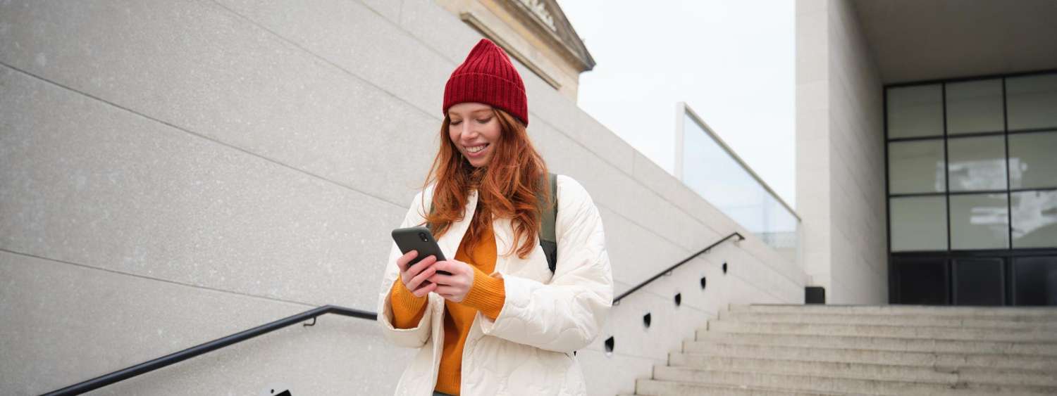 Woman in a red hat searching on her phone on city centre steps, the way most Cardiff customers find a local business