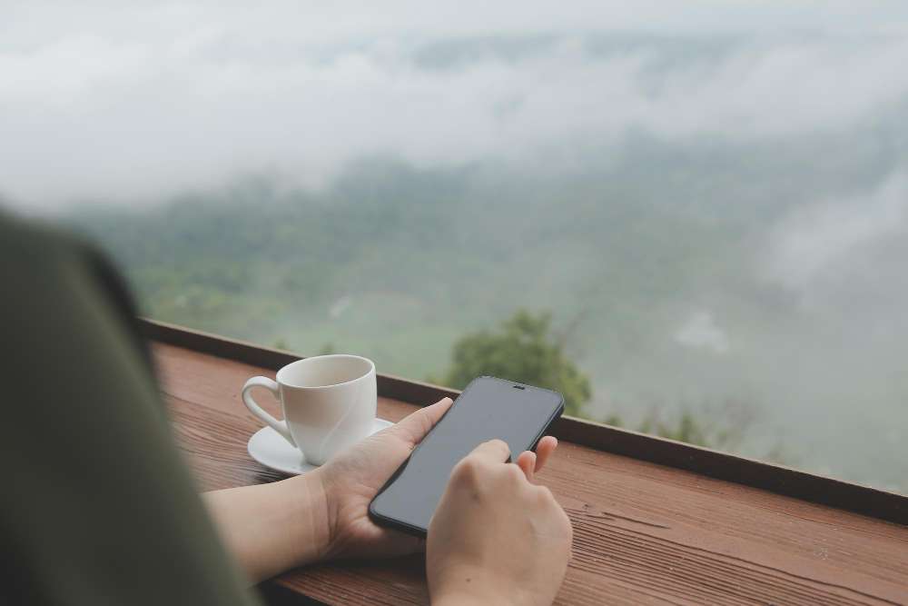 Customer searching on a phone over a cup of coffee with misty green hills outside the window