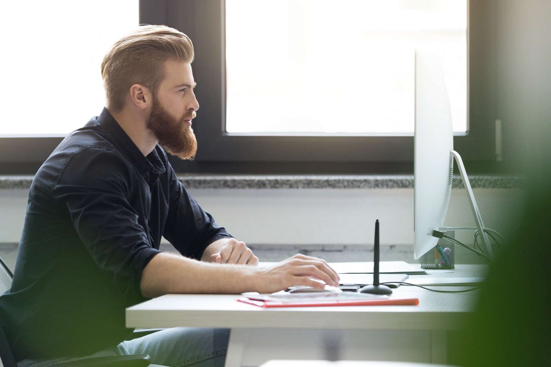 Bearded man at a desktop computer by a window, managing a Google Ads account