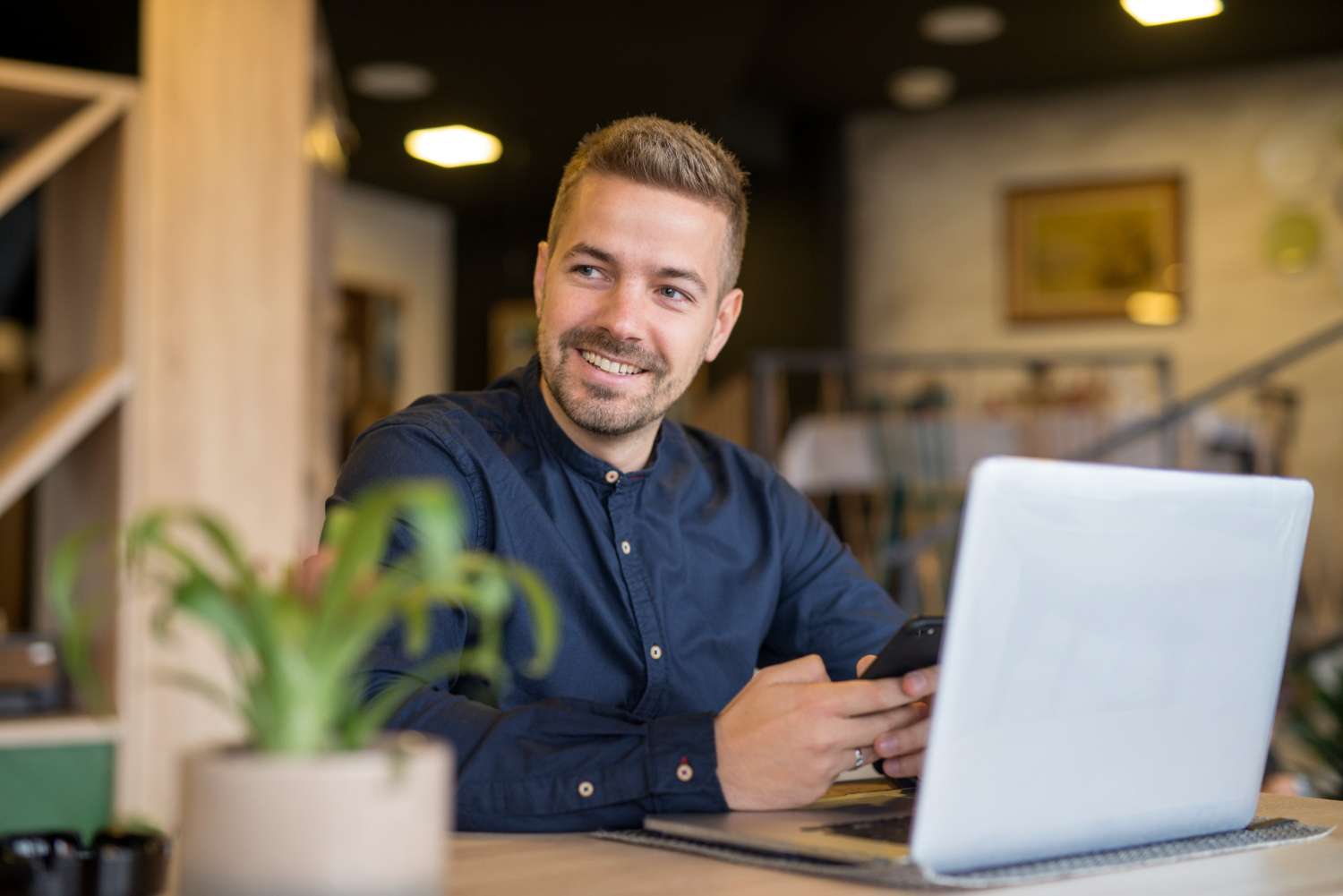 Smiling man with a phone and laptop in a café checking how his Newport business shows up on Google