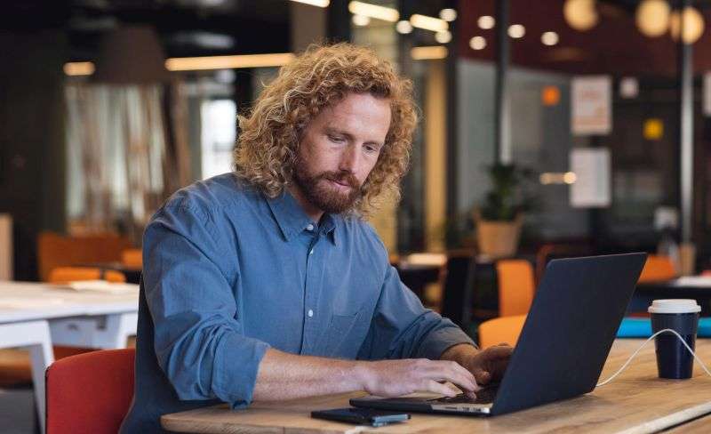 Man working through SEO Bridgend questions on a laptop at a table in a busy office