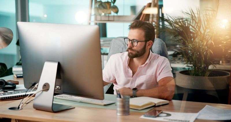Man in a pink shirt and glasses working through a Newport SEO plan on a desktop computer